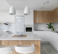 Kuchyně ve vile s bílými a dřevěnými skříňkami, osvětlená moderními lampami.
