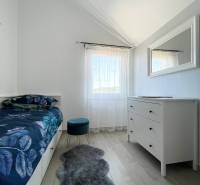 Ložnice v rekreačním apartmánu s postelí, bílou komodou a křeslem na dřevěné podlaze.