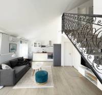 Obývací prostor v rekreačním apartmánu s kuchyní, sedačkou a schodištěm.