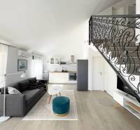Obývací pokoj s pohovkou, kuchyňským koutem a ozdobným zábradlím, v rekreačním apartmánu.