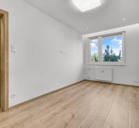 Prázdná místnost s dřevěnou podlahou a plastovým oknem ve 4-pokojovém bytě.