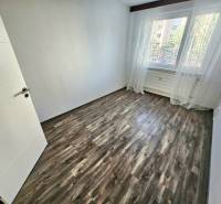 Prázdný pokoj s laminátovou podlahou a velkým oknem ve 3-pokojovém bytě.