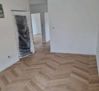 Neúplně dokončený prostor ve 4-pokojovém bytě s položenou dřevěnou podlahou.