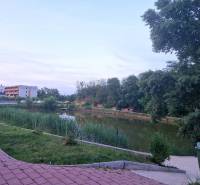 Jezero s chodníkem v Senci, ulice Vtáčí, mezi stromy a obytnými budovami.