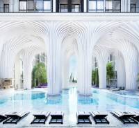 Luxusní výstavba bytů s bazénem a bílými sloupy připomínající futuristickou architekturu.