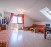Rekreační apartmán s oranžovou sedací soupravou a jídelním stolem pod střešním oknem.