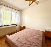 Ložnice s postelí, oknem a dřevěnou podlahou v rodinném domě.
