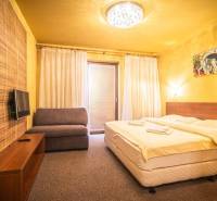 Ložnice v rekreačním apartmánu s manželskou postelí, pohovkou a televizí.