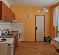 Kuchyně v 2-pokojovém bytě s oranžovými stěnami, dřevěnou podlahou a jídelním stolem.