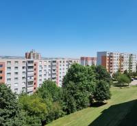 Sídliště s paneláky na Petzwalově ulici v Nitře, obklopené zelení a modrou oblohou.