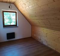Podkrovní místnost s dřevěným obkladem, oknem a jednoduchým osvětlením v chatě.