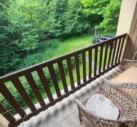Balkon chaty s proutěnými židlemi a výhledem na zahradu a zeleň.