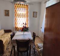 Jídelna v rodinném domě se stolem, židlemi, květinami, kobercem a závěsem.