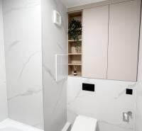 Minimalistická koupelna v 2-pokojovém bytě s WC, vanou a úložnými prostory.