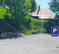 Parkoviště na ulici Donovaly ve městě Donovaly u rodinných domů, se stromy a trávou.