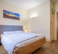 Světlá ložnice rekreačního apartmánu s manželskou postelí, nočními stolky a dekorací na stěně.