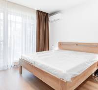 Světlá ložnice s dřevěnou postelí a nočním stolkem ve 2pokojovém bytě.
