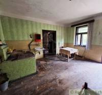 Kuchyně v rodinném domě s jednoduchým zařízením, dřevěná podlaha a zelené stěny.