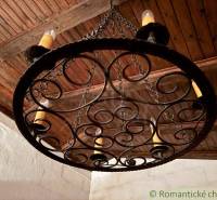Kovaná lampa se svíčkami v interiéru rodinného domu s dřevěným stropem.