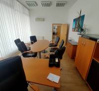 Kanceláře vybavené nábytkem s kulatým stolem, křesly a skříněmi.