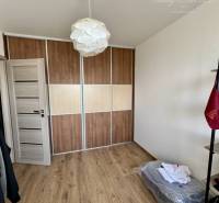 Pokoj čtyřpokojového bytu s dřevěnou podlahou, vestavěnou skříní a bílým svítidlem.