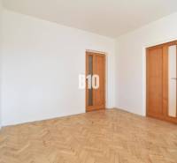 Bílé stěny a dřevěné parkety v místnosti 4pokojového bytu.