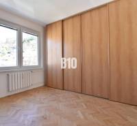 Pokoj ve 4pokojovém bytě s dřevěnou podlahou, vestavěnou skříní a výhledem do exteriéru.