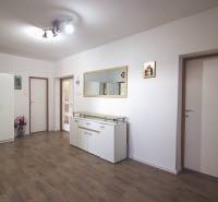 Interiér rodinného domu s bílým nábytkem, podlahou s dřevěným dekorem a velkým zrcadlem.