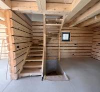 Dřevěný interiér chaty s betonovou podlahou a schodištěm.
