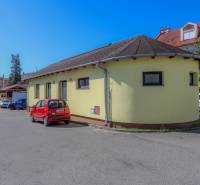 Žlutá budova na ulici Slovenského národního povstání ve městě Vrbové s parkujícím červeným autem.