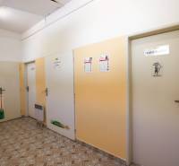 Chodba s dveřmi v obchodních prostorách, světlé stěny a dlažba na podlaze.