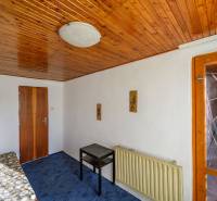 Dřevěný strop, postel, stolek, modrý koberec, lampa na stěně v chatě.