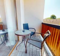 Balkon v 2-pokojovém bytě s výhledem na okolní zeleň a střechy.