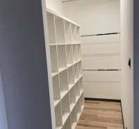 Vestavěná skříň s policovým systémem v 3-pokojovém bytě, světlé dřevěné podlahy, bílé stěny.