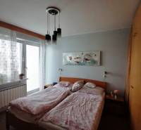 Ložnice v rodinném domě s manželskou postelí, skříní a balkónovými dveřmi.