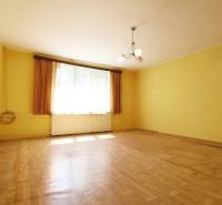 Pokoj v rodinném domě se žlutými stěnami, dřevěnou podlahou a centrálním lustrem.