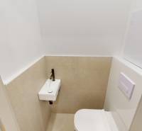 Kompaktní WC s umyvadlem v 2pokojovém bytě, béžové dlaždice a bílá stěna.