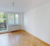 Prostorný pokoj v 2pokojovém bytě s dřevěnou podlahou a velkým oknem na balkon.
