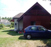 Auto zaparkované u chaty v Klížské Němé, obklopené zeleným trávníkem a stromy.