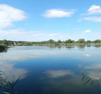 Jezero u Klížské Něme obklopené stromy a rákosím s klidnou oblohou.