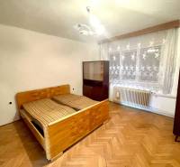Interiér rodinného domu s dřevěnou podlahou, postelí a záclonami na okně.