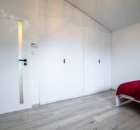 Ložnice v rodinném domě s bílou skříní, dveřmi a postelí s barevnou přikrývkou.