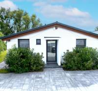 Rodinný dům v Černé Vodě s bílou fasádou, obklopený zelení a dlažbou.