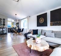 Obývací pokoj v rodinném domě s šedou sedačkou, dřevěným stolem a jídelním koutem.