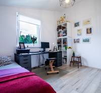 Pracovní kout v rodinném domě se stolem, postelí a policí s trofejemi.