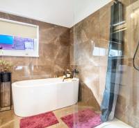 Koupelna v rodinném domě s vanou, mramorovými obklady a růžovými koberci.