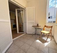 Balkon ve 2-pokojovém bytě s bílými žaluziemi a dřevěnou židlí.