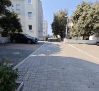 Dlázděná cesta v Novalji vede k 2pokojovému bytu, obklopená stromy a budovami.