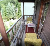 Balkon chaty v Holčíkovcích s dřevěným zábradlím a starožitným nábytkem obklopený přírodou.