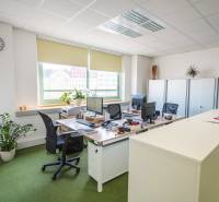 Kanceláře s pracovními stoly, počítači a zelení, vybavení pro komfortní práci.